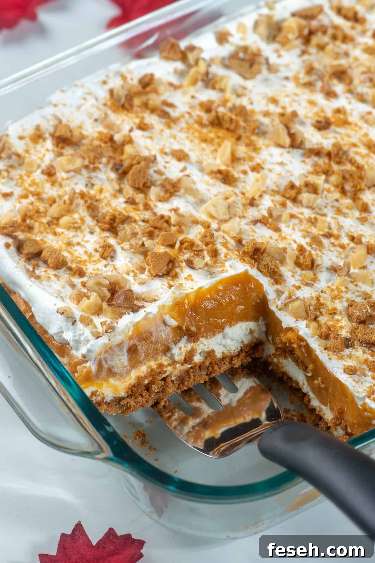 A spatula resting in a glass dish filled with layered pumpkin dessert.