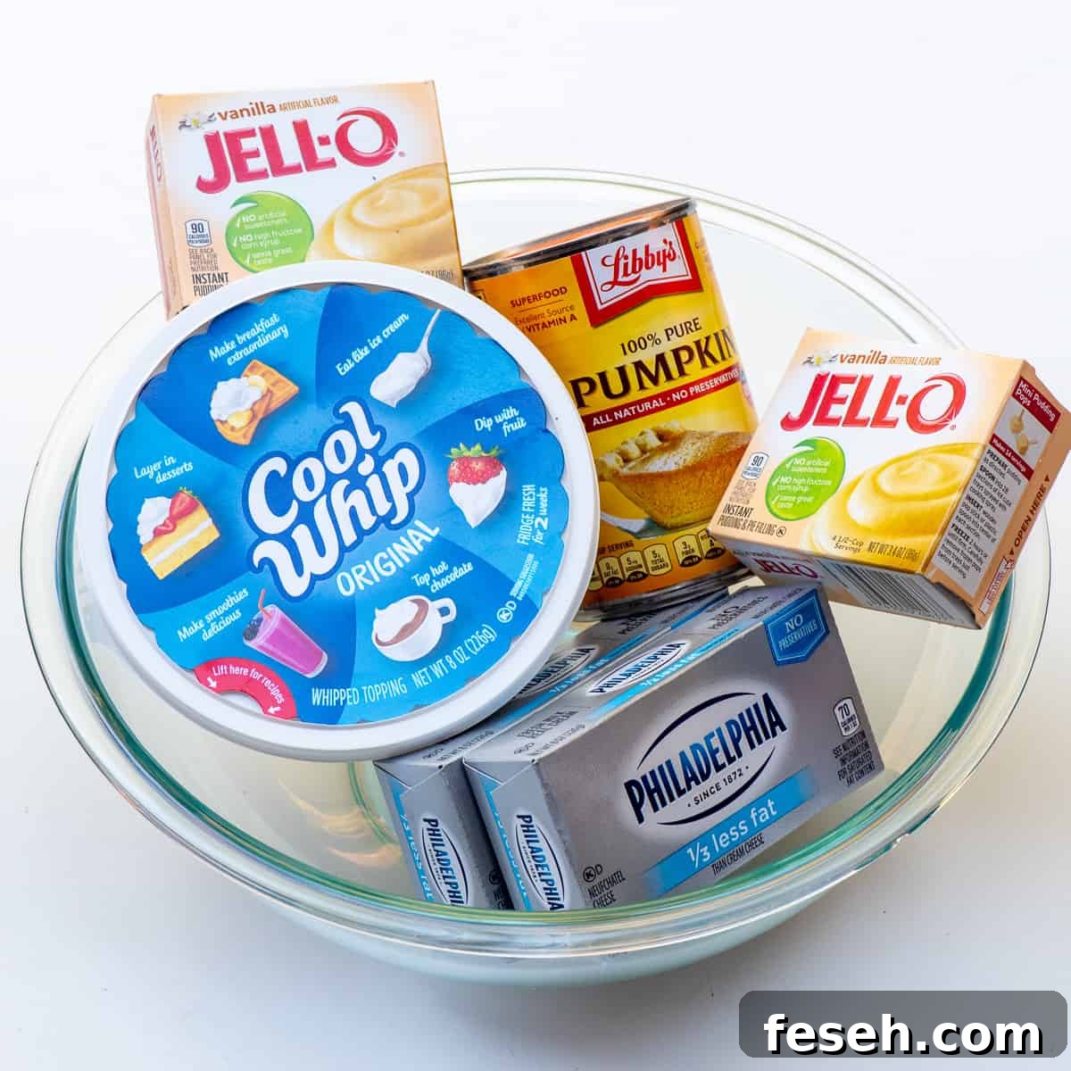 A tub of Cool Whip, can of pumpkin puree, two boxes of Jello pudding and two boxes of cream cheese in a glass bowl.