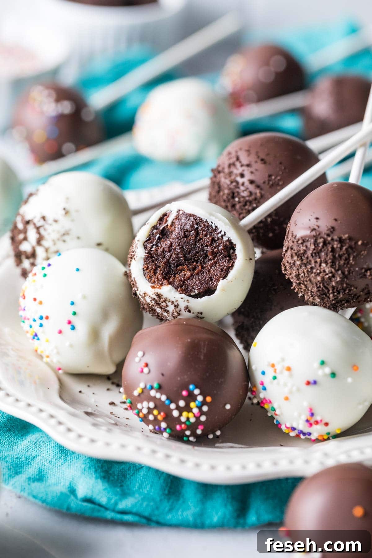 White and dark chocolate coated chocolate cake pops on a plate, with the middle pop missing a bite.