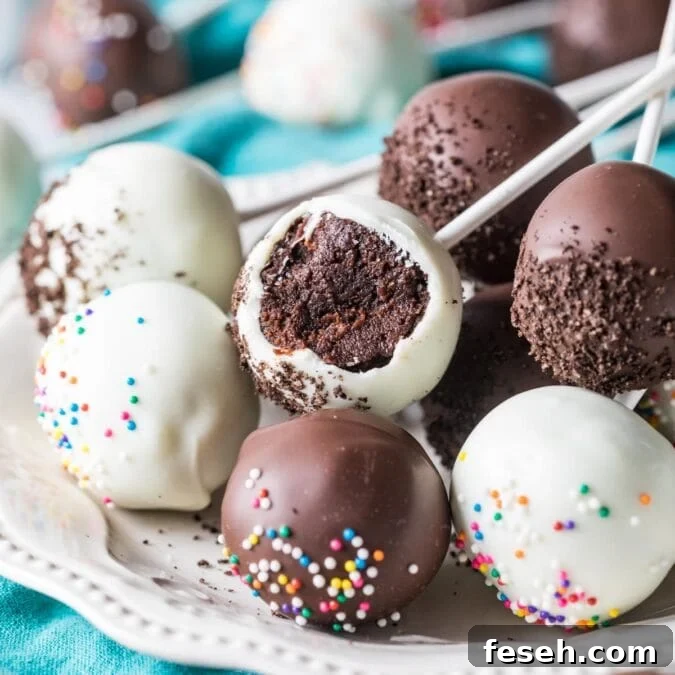 White and dark chocolate coated chocolate cake pops on a plate, with the middle pop missing a bite.