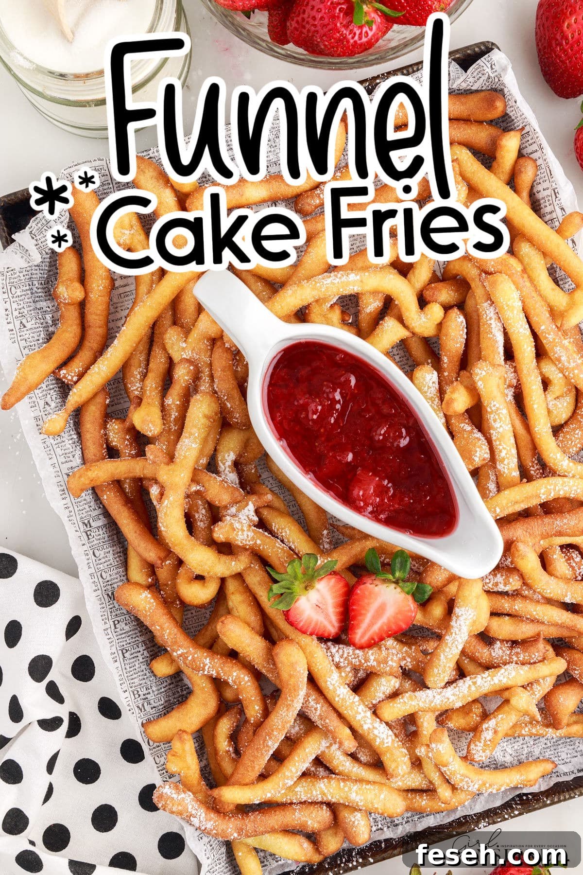 A large tray of Funnel Cake Fries on newsprint paper with a dish of strawberry sauce.