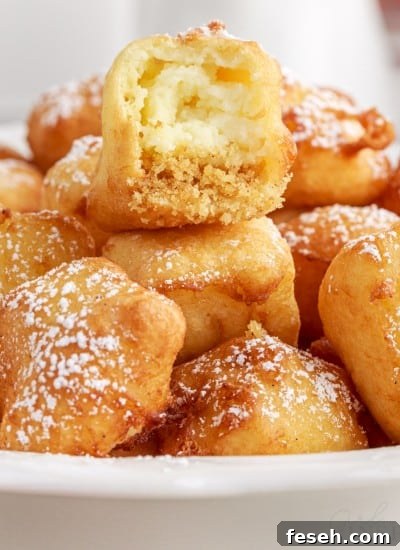 Close up of a bite taken from a fried cheesecake in a bowl of fried cheesecakes.