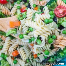 A bowl of pasta salad and a wooden spoon, zoomed in.