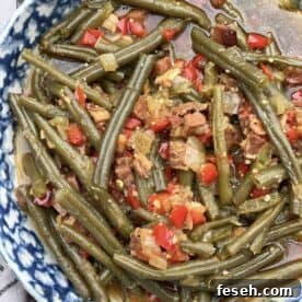 A bowl of southern style green beans cooked in a crock pot with ham, bacon, and red bell peppers.