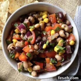 A small bowl of redneck caviar with black-eyed peas, corn, black beans, and tomatoes with a side of tortilla chips.