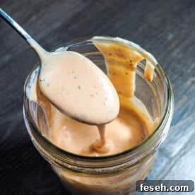 A jar of homemade raising canes sauce dripping off of a spoon.
