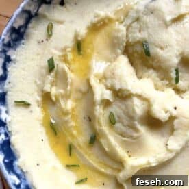 A bowl of buttermilk mashed potatoes with a pool of melted butter and fresh chives on top, zoomed in.