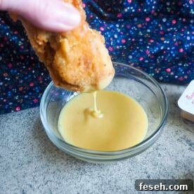 A chicken nugget being dunked into a small glass bowl of copycat chick-fil-a sauce.