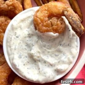 A small bowl of homemade tartar sauce with a fried shrimp in it.