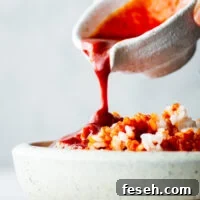 Spicy bibimbap sauce poured over a bowl of steamed white rice.