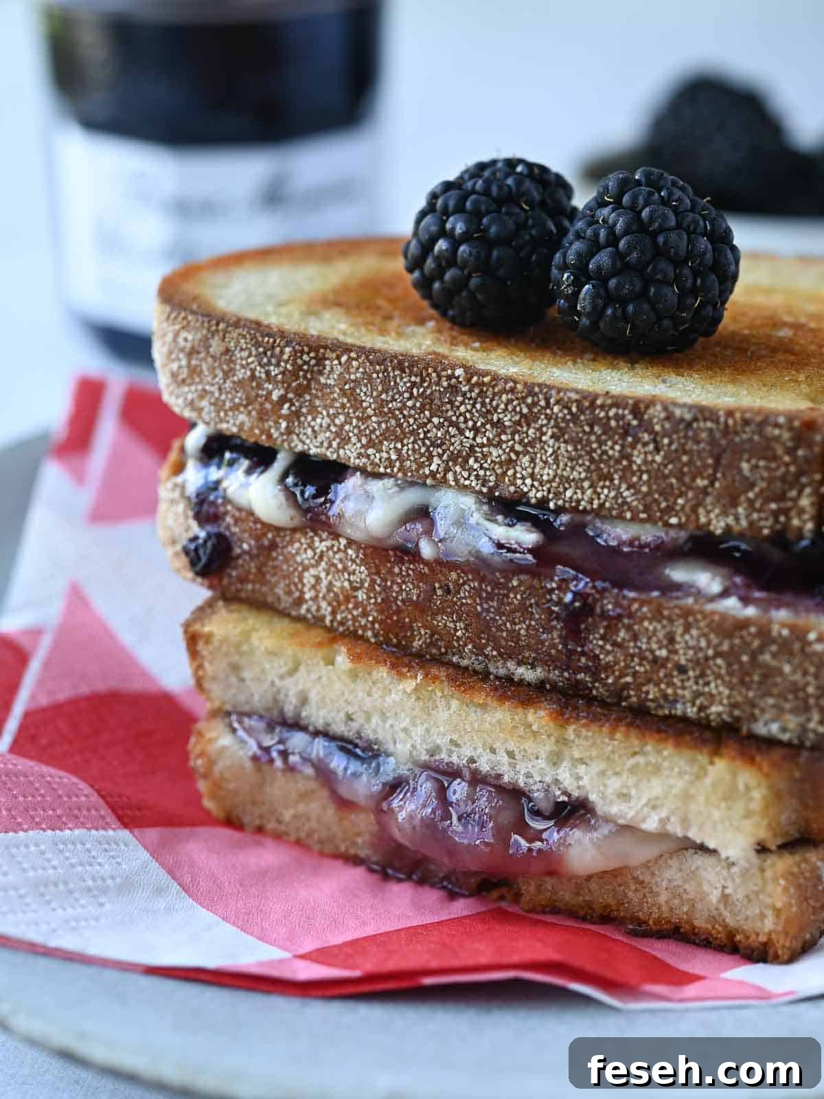 Blackberry Boursin grilled cheese stacked on a white plate with a red checkered napkin underneath.