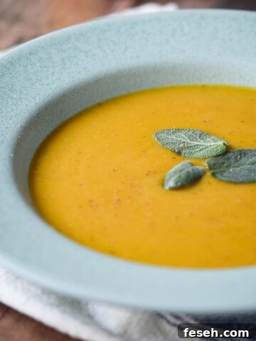 Close-up of butternut squash soup in a blue bowl with sage on top.