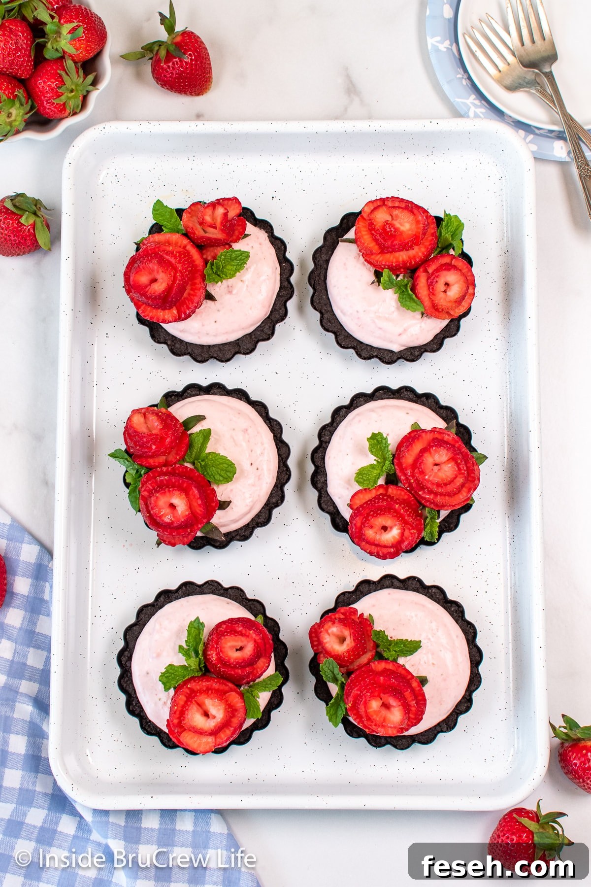 Six mini strawberry tarts topped with berries on a white pan.