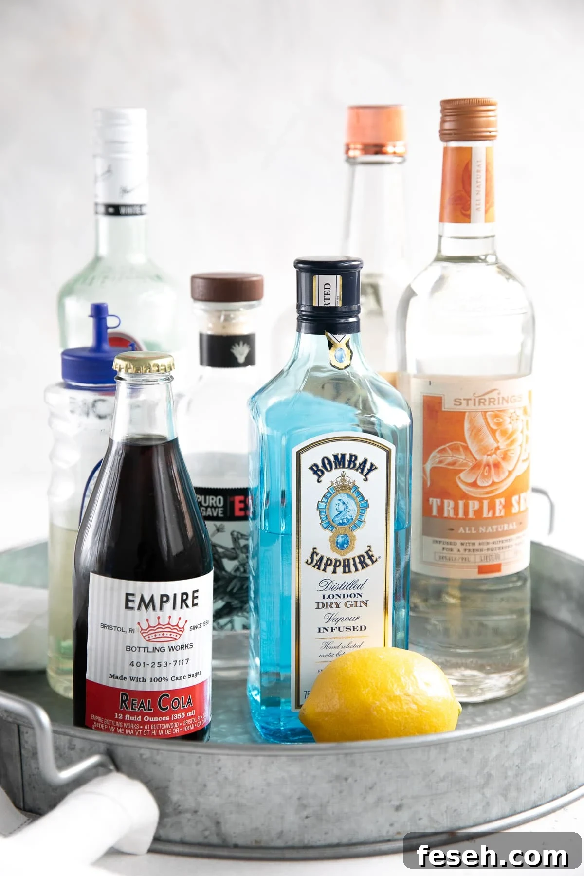 All the ingredients needed to make a Long Island Iced Tea on a round metal serving tray.