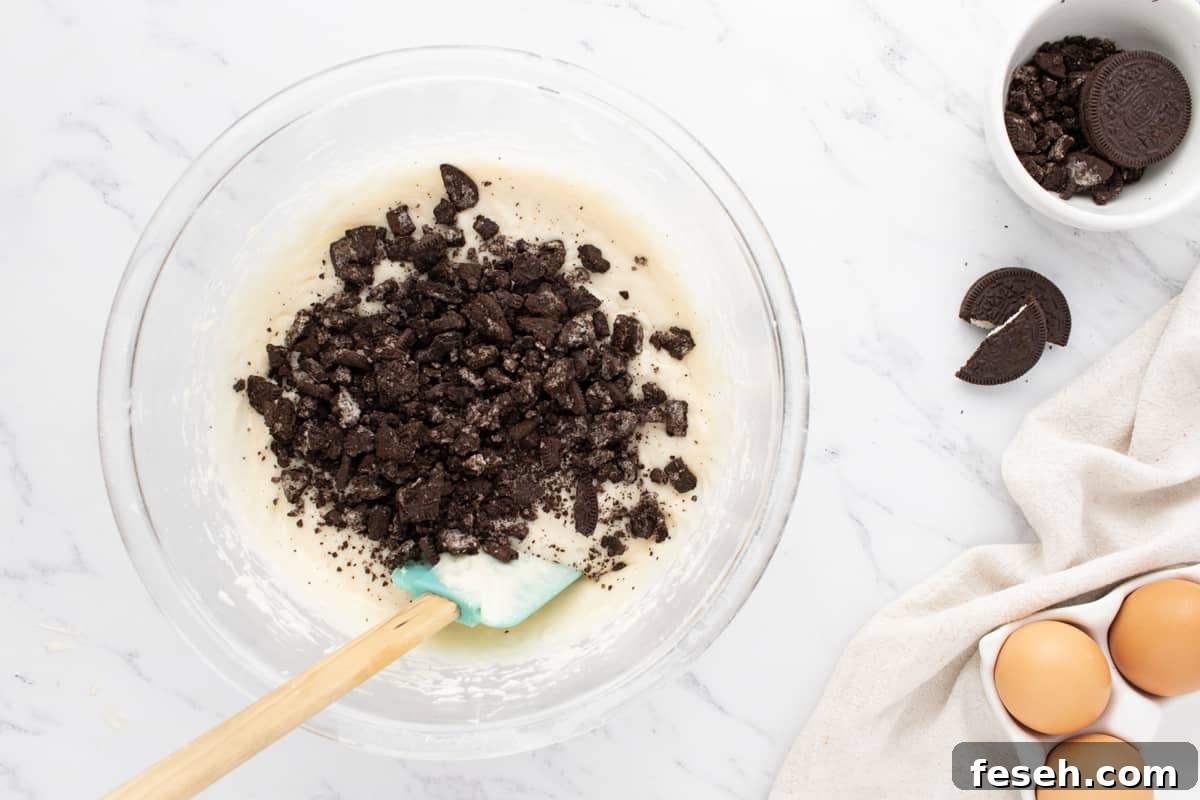 folding chopped oreo pieces into white cupcake batter with a rubber spatula.