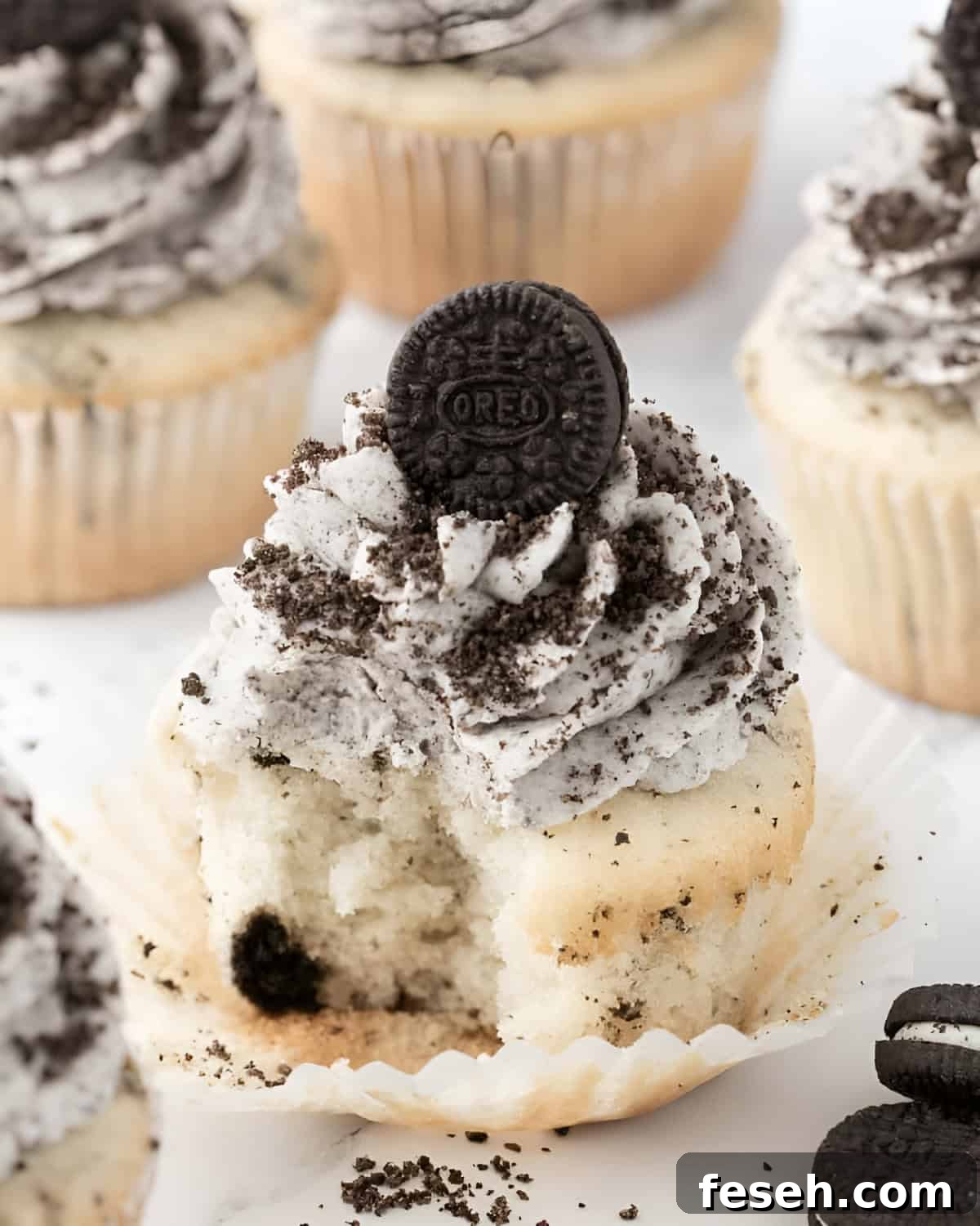 an unwrapped and bitten cookies and cream cupcake topped with Oreo crumbs and a mini Oreo cookie.