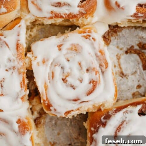 A close up of brioche cinnamon rolls with heavy cream, some are covered in a cream cheese glaze.