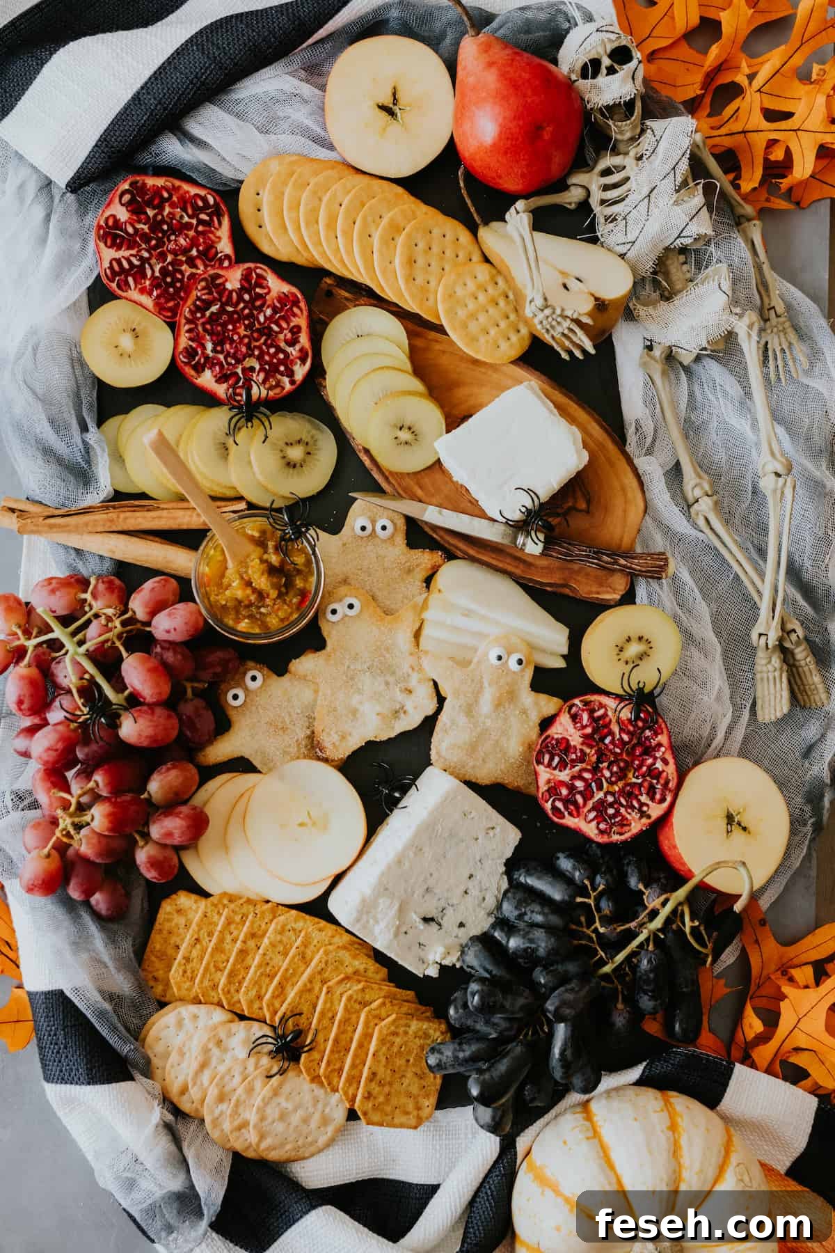 Halloween cheese board filled with fresh fall fruits, assorted cheeses, crackers, and spooky buñuelo ghosts on a black slate tray.