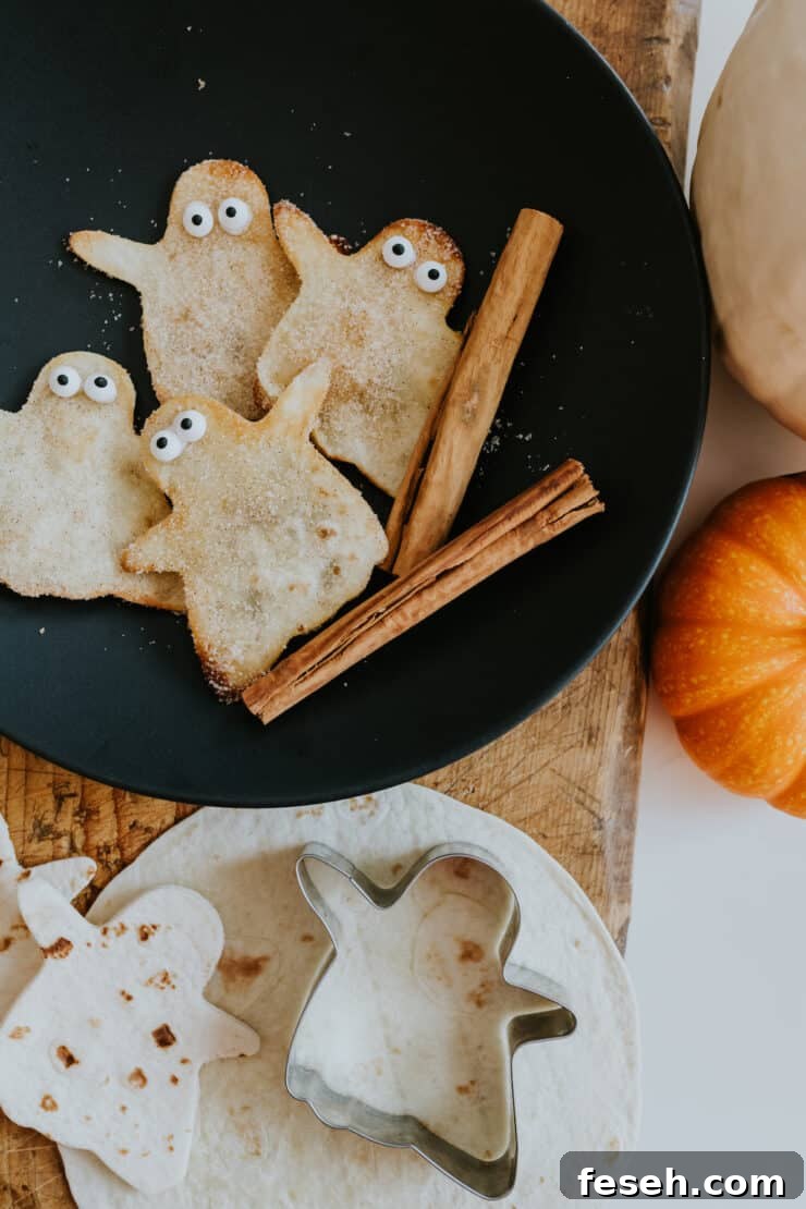 Cinnamon-sugar coated fried buñuelo ghosts arranged on a black plate with candy eyeballs.