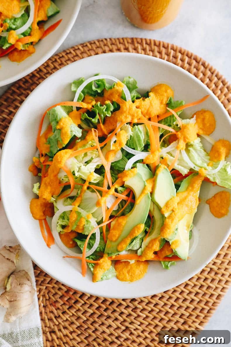 lettuce with onion, carrots, avocado in a white plate topped with a ginger dressing.