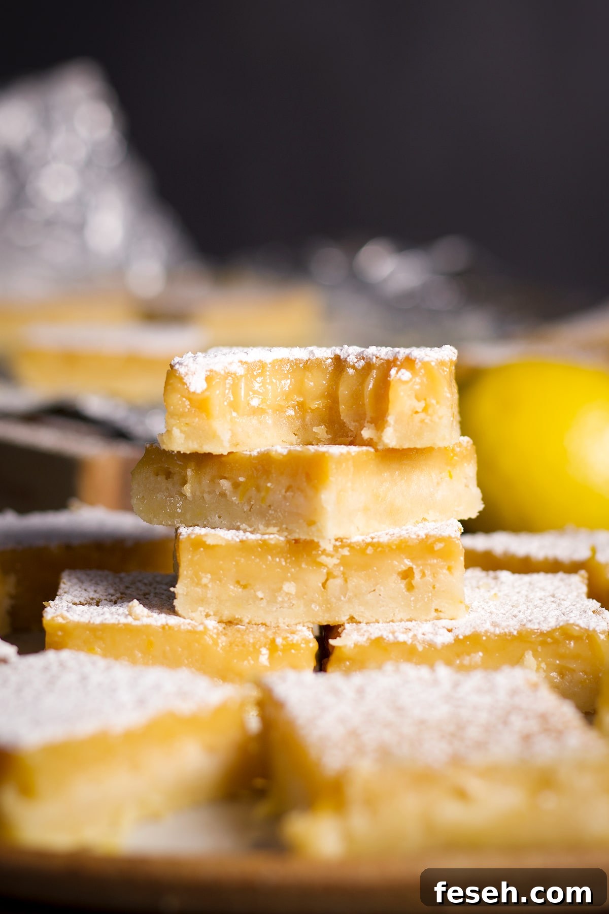 A stack of lemon bars on a plate with a bite taken out of the bar on the top of the stack.