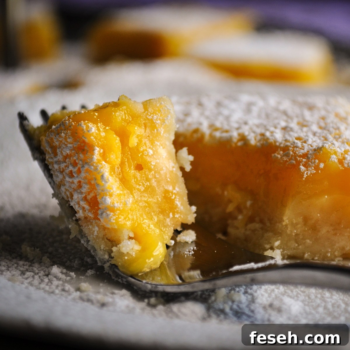 Someone using a fork to cut a bite from a lemon bar.