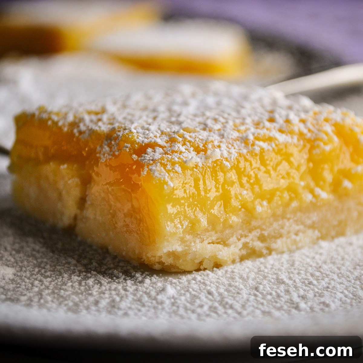 A lemon bar that's been dusted with powdered sugar resting on a white plate.