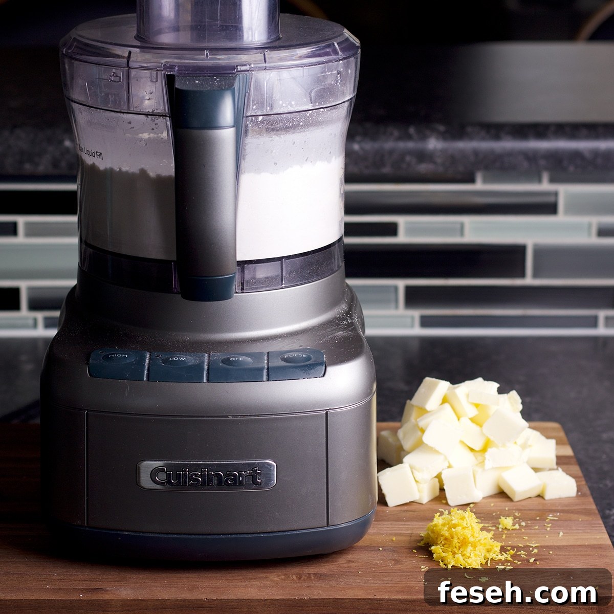The ingredients needed to make a shortbread crust for lemon bars on a countertop next to a food processor.