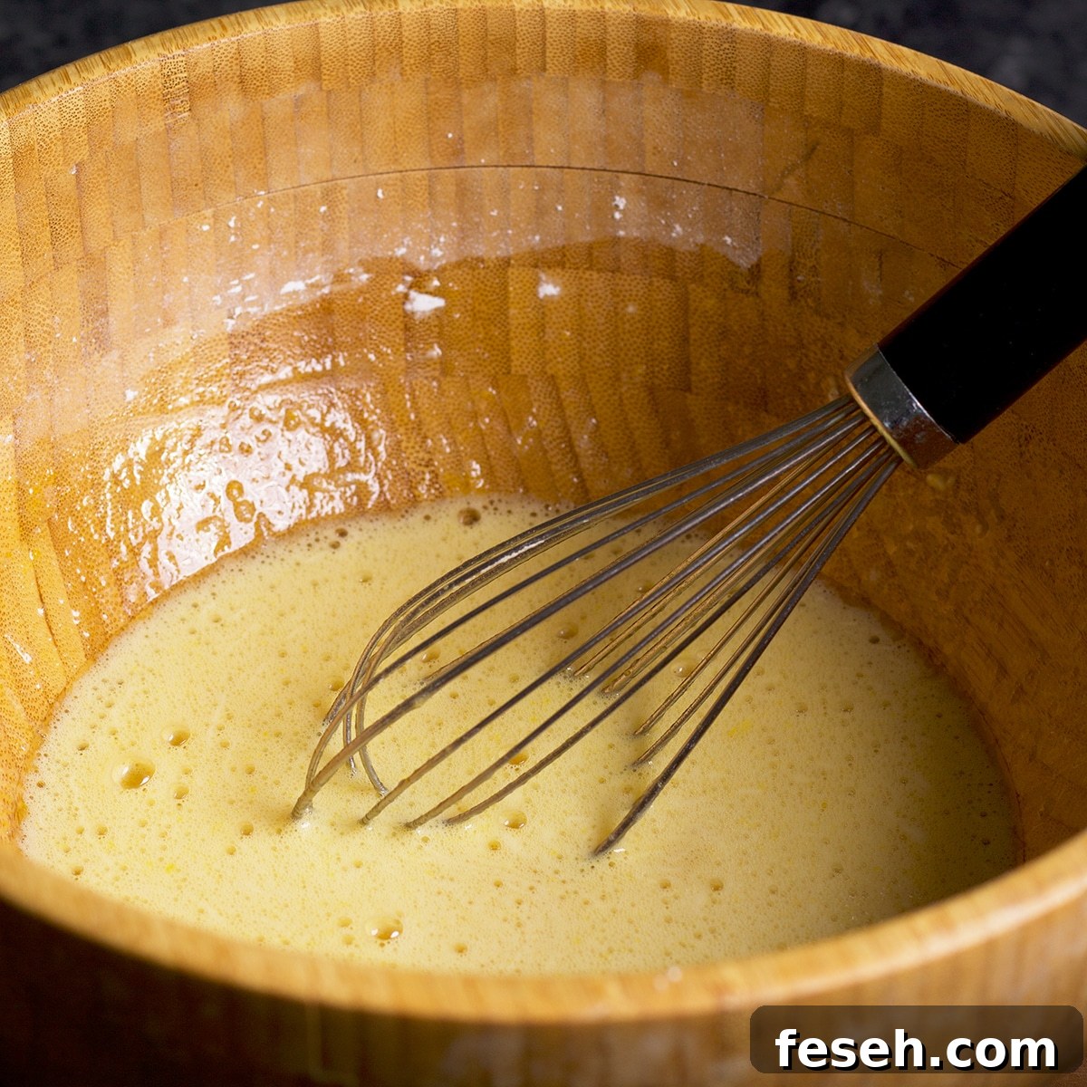 Whisking eggs, sugar, and flour in a wood bowl to make the batter for lemon bars.