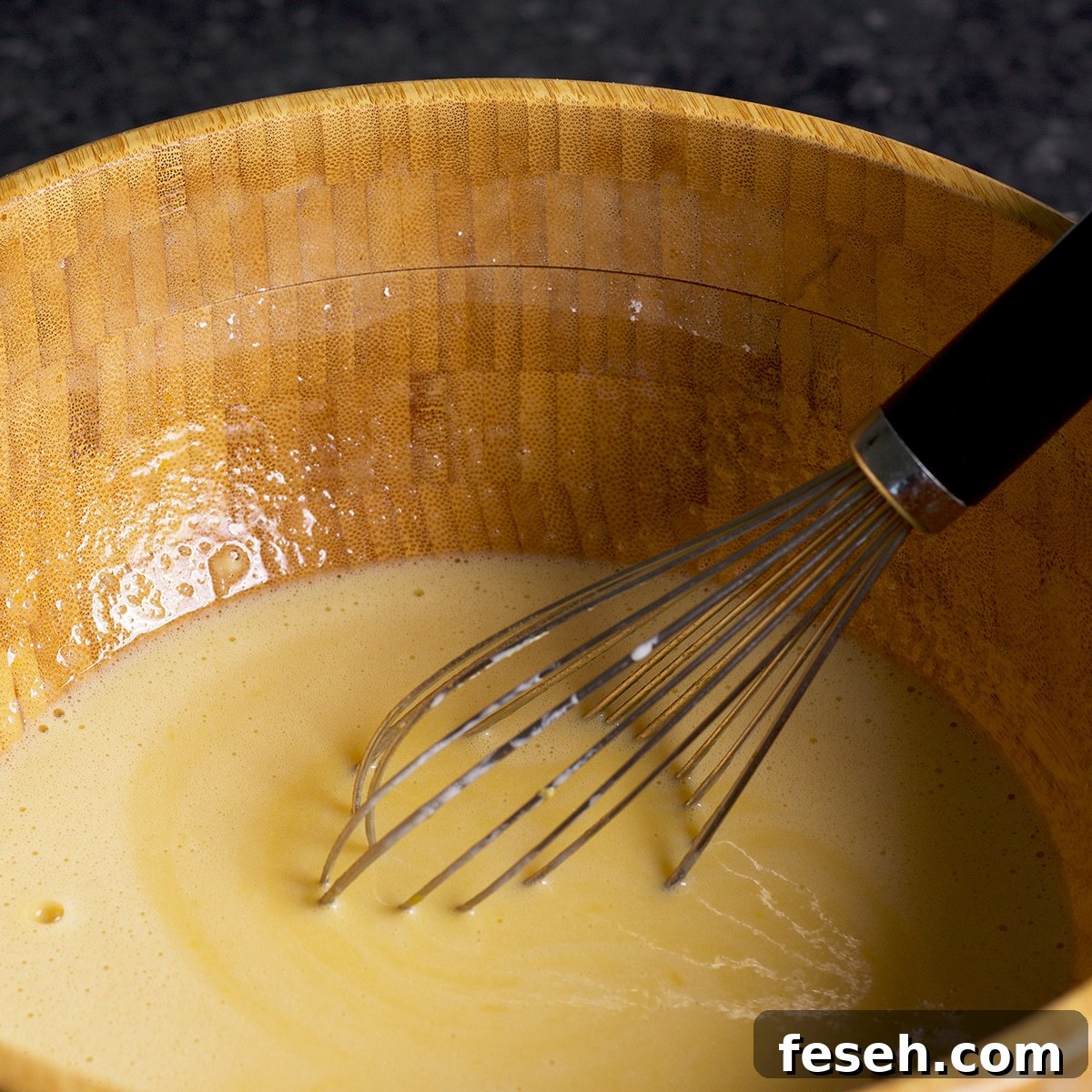 Whisking all the ingredients for lemon bars in a wood bowl.