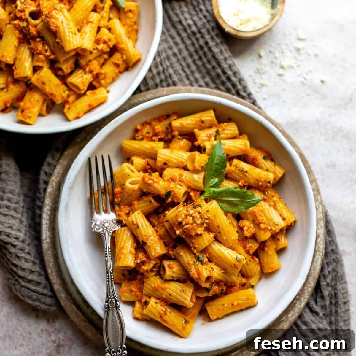 Two white bowls with a silver fork ad red pesto and a sprig of basil. 