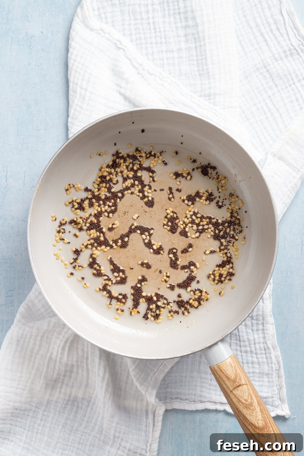 An overhead image of sauteing mustard seeds and a tablespoon of urad dal in a medium skillet.