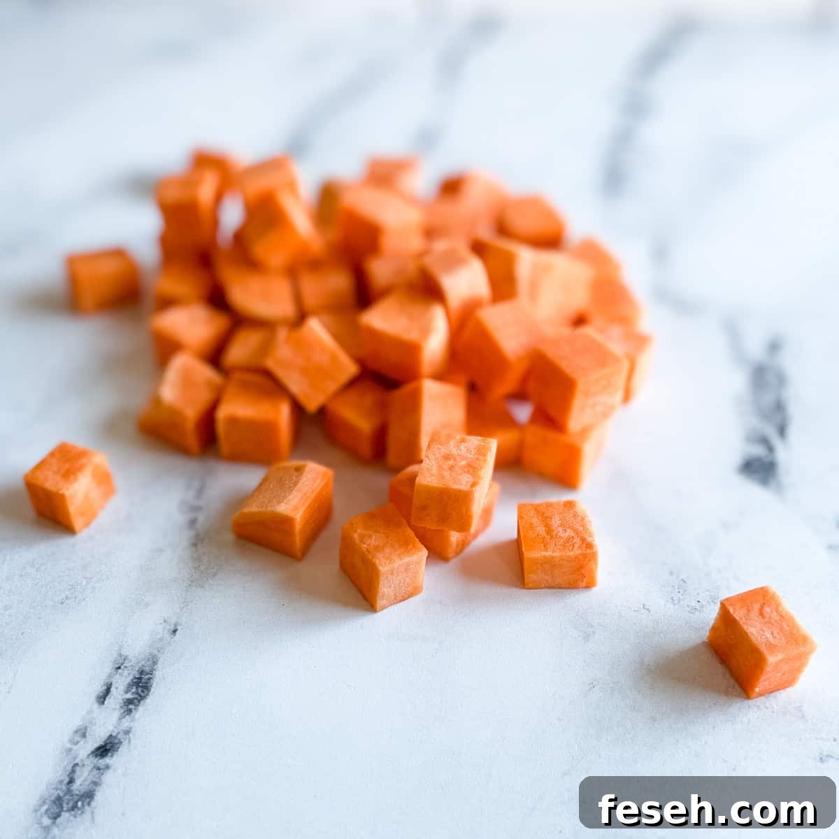 A pile of sweet potato cubes sits on a white marble counter top.