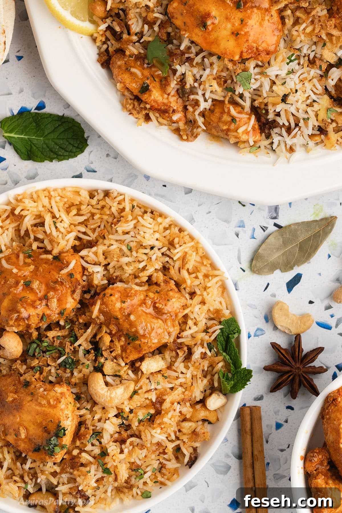 An overhead image of two chicken tikka biryani plates with spices like star anise and cinnamon sticks on the board.