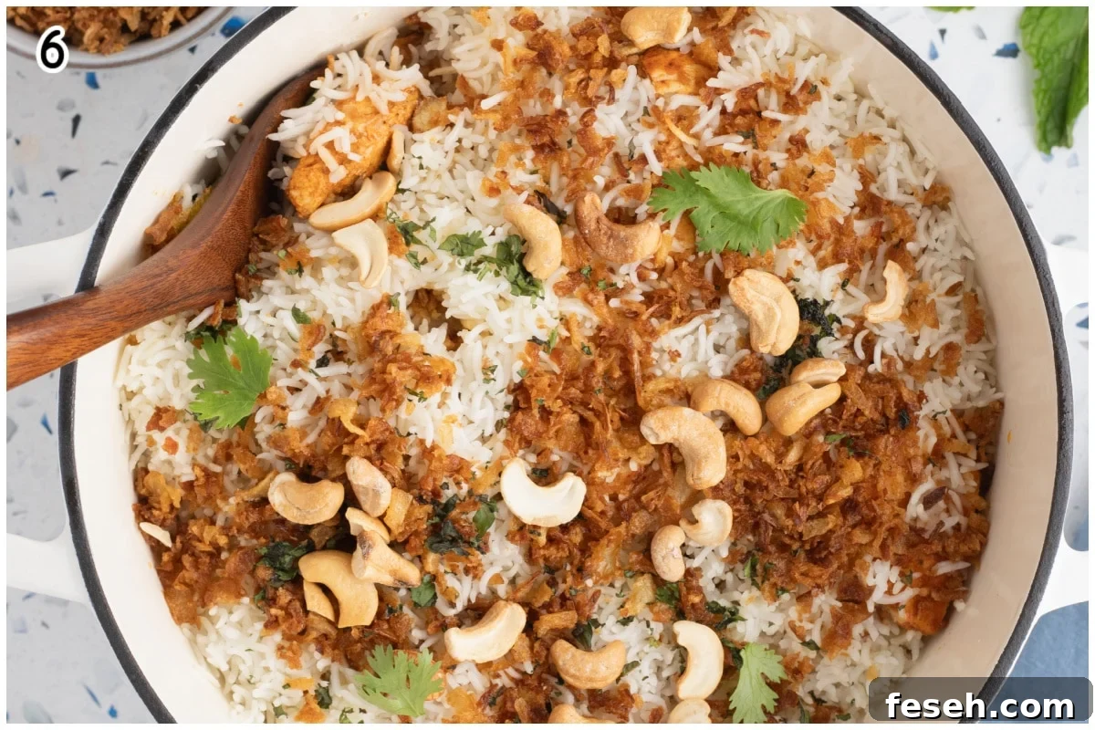 An overhead image of a large dutch oven with chicken tikka biryani with a wooden spoon.