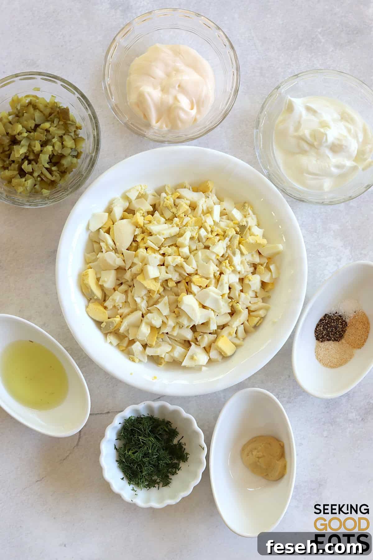 Ingredients needed to make egg salad with dill pickles on a white marble countertop.