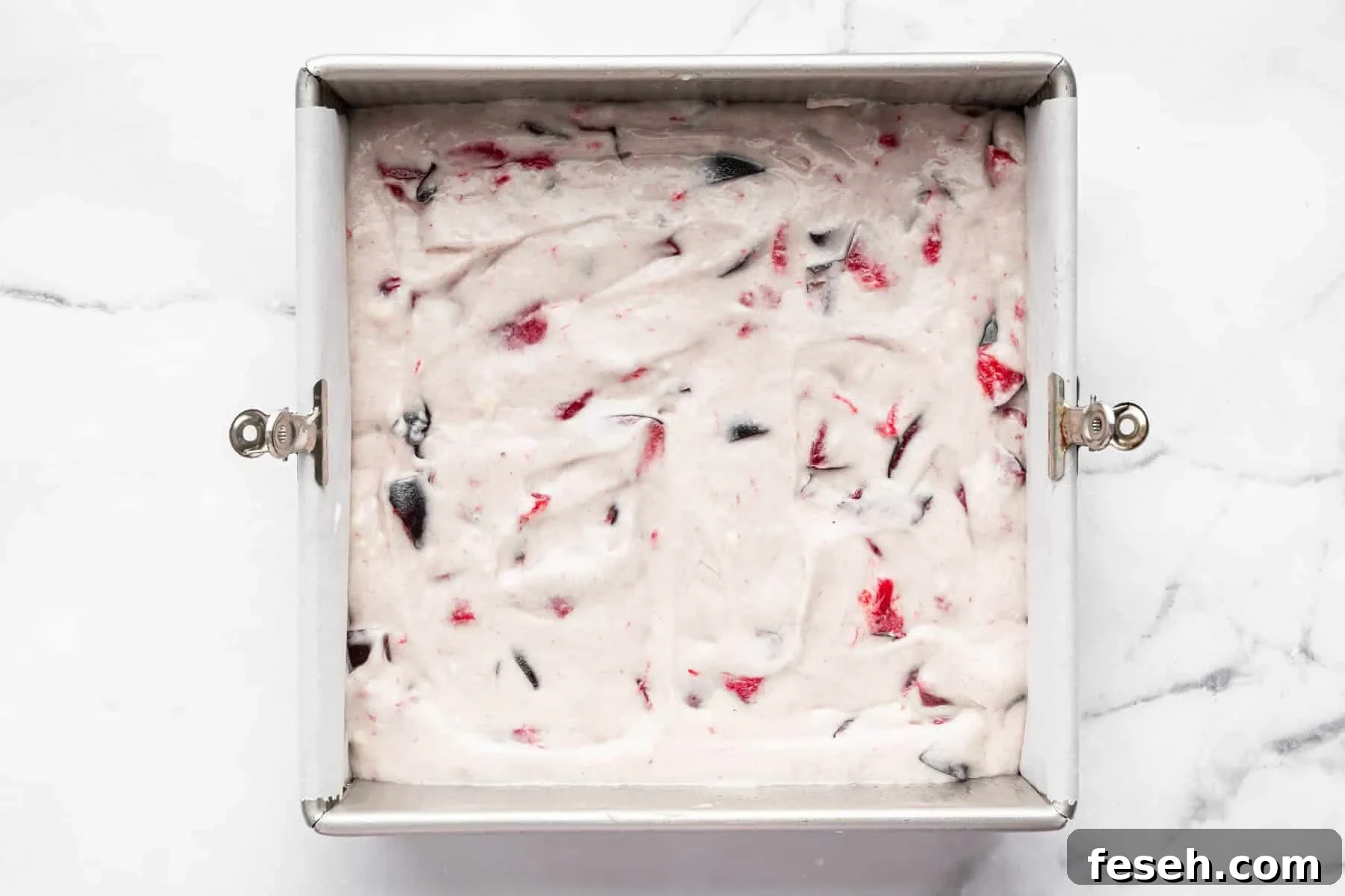 White raw batter in a square pan with chunks of red and purple fruit.