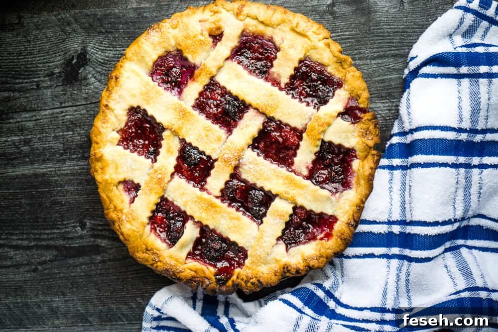 blackberry raspberry pie with lattice top on wooden surface next to blue and white plaid tea towel