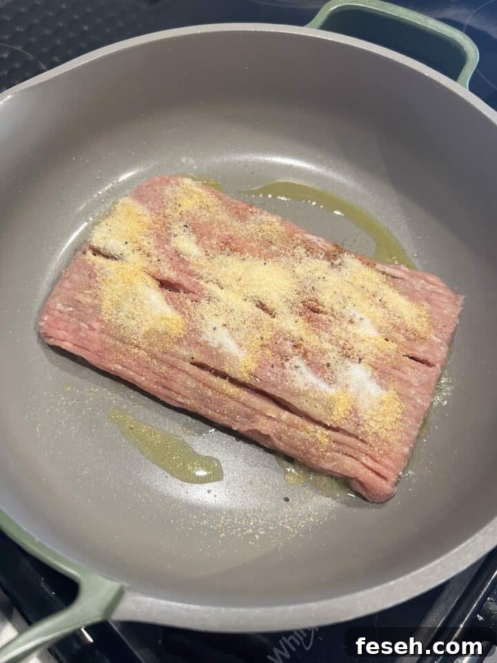 Raw ground chicken added to a large skillet with seasonings