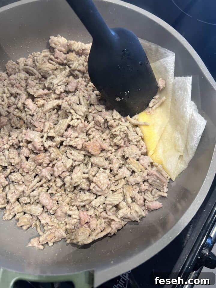 Crumbled and cooked ground chicken in a pan, with a piece of paper towel absorbing excess oil