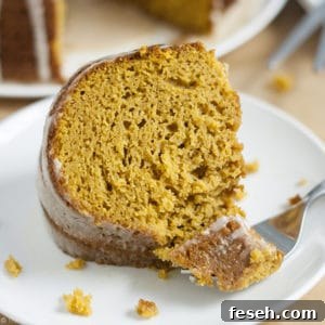 An image of a slice of pumpkin cake with a fork in front of it holding a bite of the cake on it.