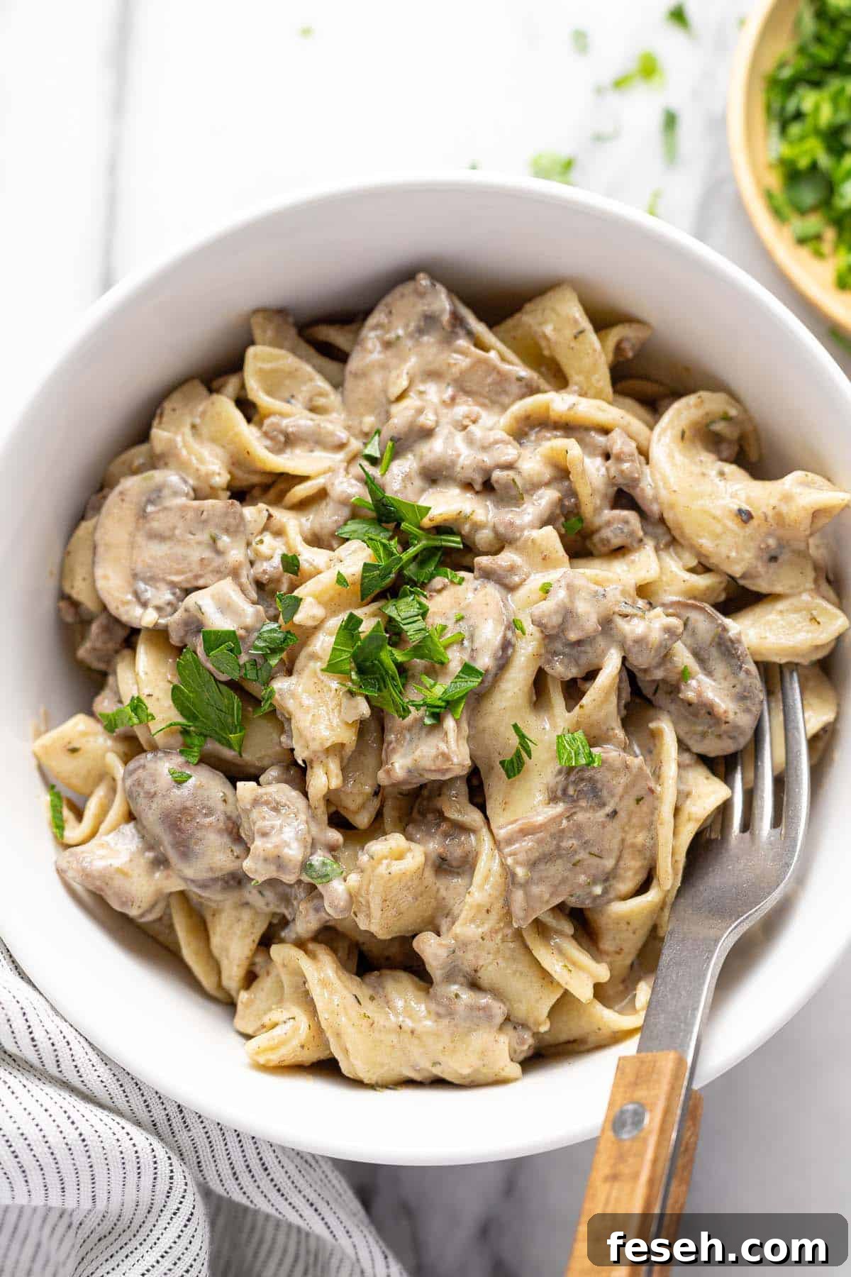 Bowl of ground beef stroganoff and egg noodles garnished with parsley. 
