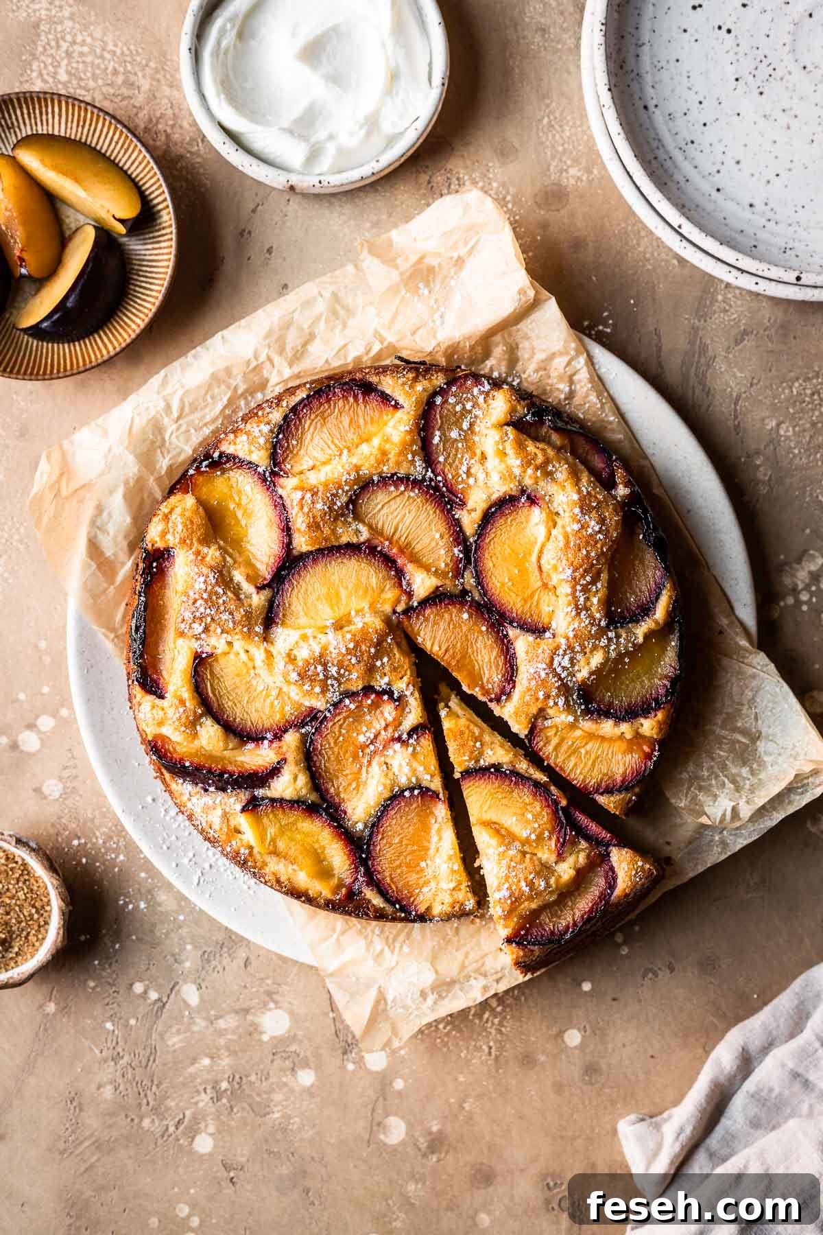 Baked plum cake on a parchment lined plate with a slice cut.