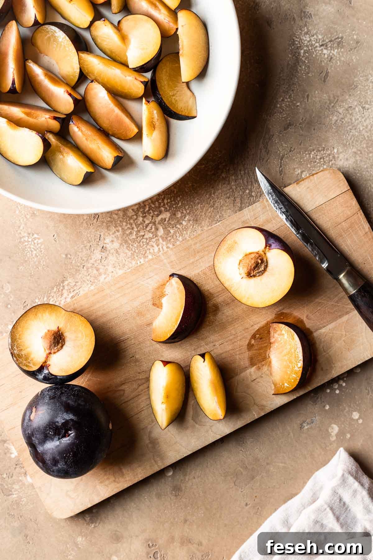 Sliced plums on a wooden cutting board with more on a plate nearby.