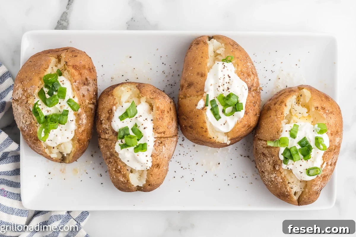 Smoked baked potatoes on a white platter topped with sour cream and chives