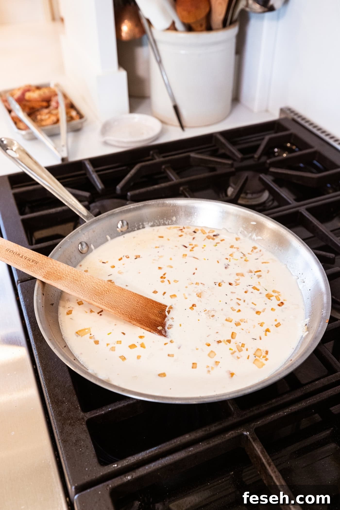 Metal skillet on a stovetop with cream and browned pieces of rice and onion being stirred together with a wooden spatula.