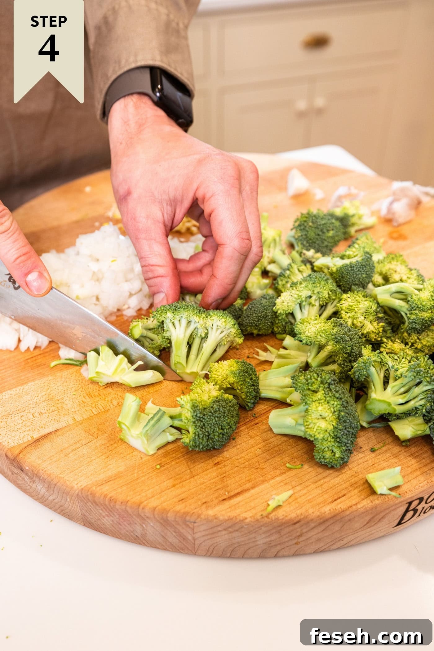 Hand using a knife to chop broccoli into smaller pieces on a wooden cutting board.