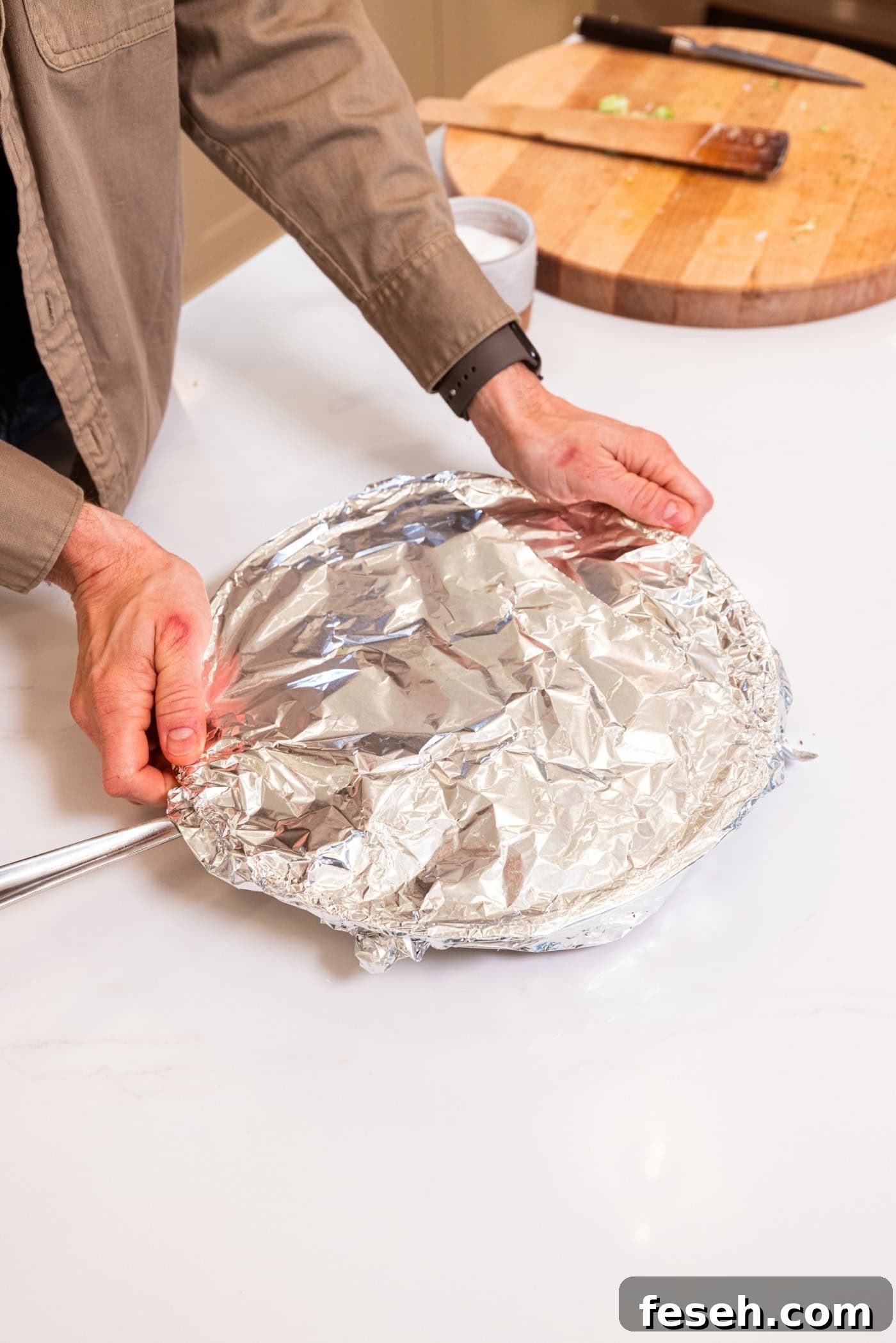 Two hands placing aluminum foil over the top of a skillet with chicken.
