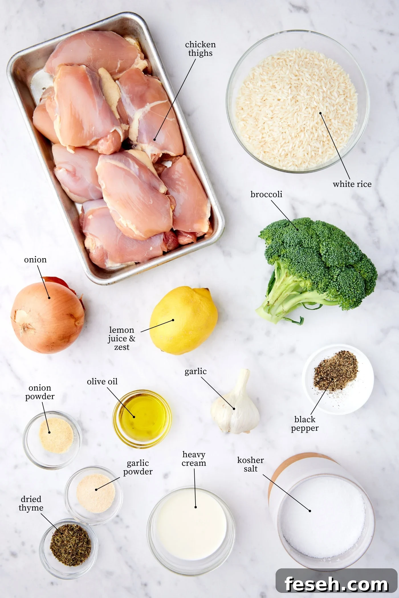 White marble surface filled with ingredients needed to make chicken, broccoli, rice casserole including raw chicken, broccoli, rice, onion, lemon, spices, and more.