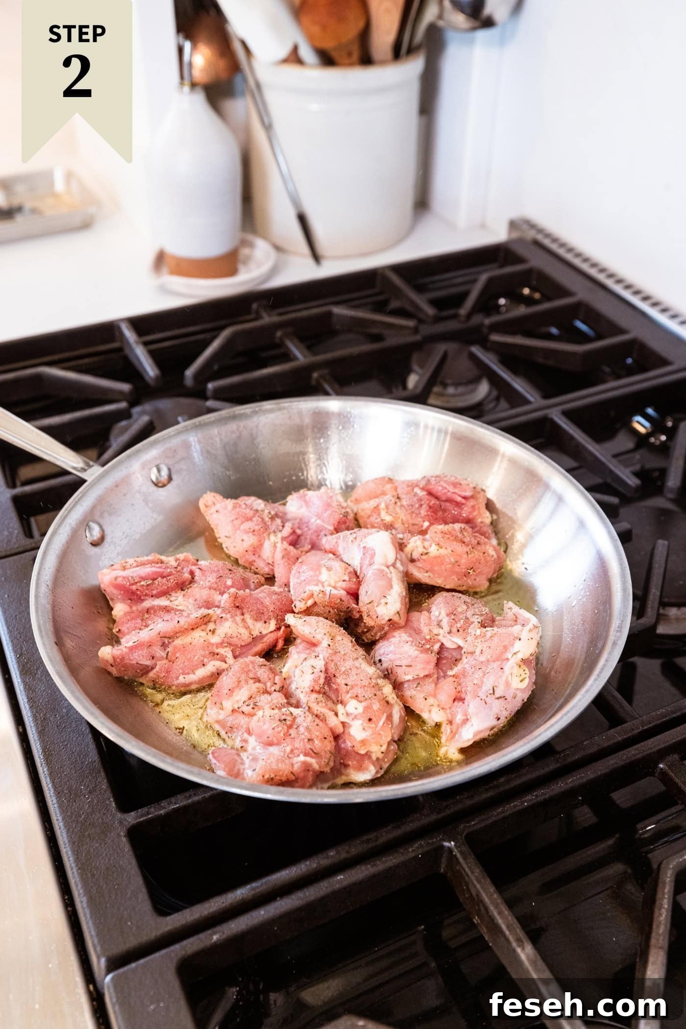 Raw marinated chicken thighs in a metal skillet on the stovetop browning on one side.